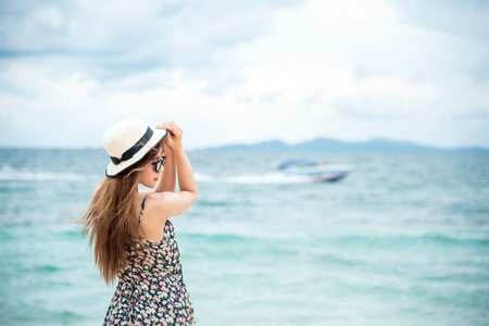 Cheerful asian woman barefoot walking on tropical summer beach. Woman walking along wave of sea water and sand on the beach. Enjoyment barefoot walk outdoor with freedom. Relaxation Travel Concept.の写真素材