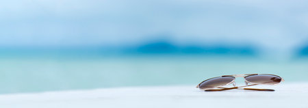 Banner Sunglasses on summer beach vacation time to travel. Tropical summer beach with sea wave in sunshine day. Fashionable outdoor sunglasses accessory blue sea on seaside. Summer tropical sandy sunlight with copy spaceの写真素材