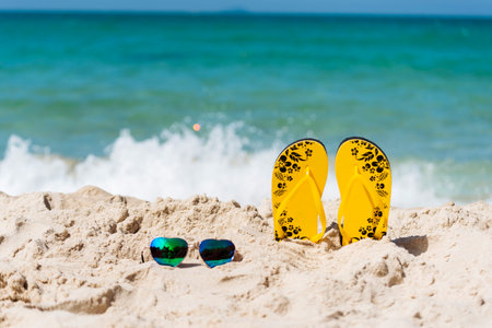 Yellow Sandal rubber shoe on the beach vacation time to travel. Tropical summer beach with sea wave in sunshine day. Slipper shoes outdoor with white wave blue sea on the beach. Summer tropical beachの写真素材