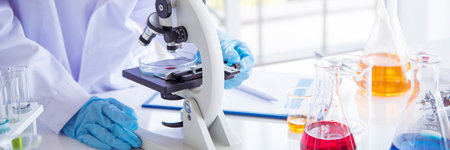 Banner Asian woman scientist hand write note research in medical lab look at science microscope. Panorama biology chemistry lab. Asian Female technician laboratory using microscope with copy spaceの写真素材