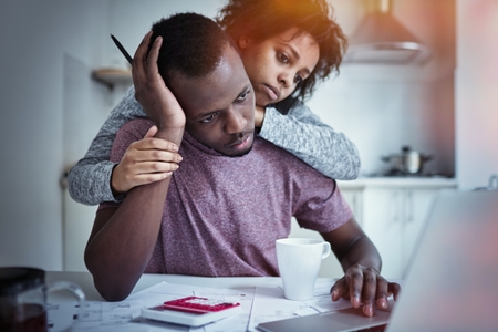 Close up portrait of young unhappy african american couple sitting at kitchen table in front of open laptop computer while paying bills online, using banking application, having concentrated looksの写真素材