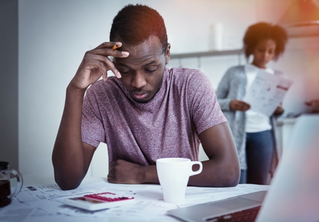 Unhappy african american family financial stress: black man sitting at kitchen, reading notification informing that bank denied to prolong loan term, his wife standing with bills in backgroundの写真素材