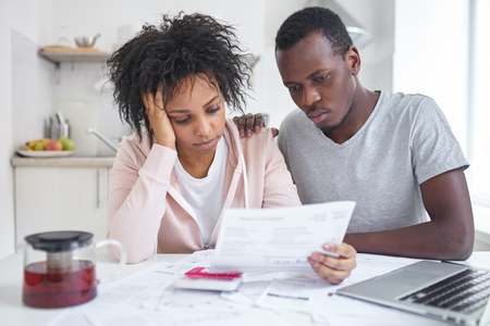 Depressed bankrupt young african american family sitting at kitchen table, feeling stressed while reading notification, informing about eviction from their appartment because housing debt. No moneyの写真素材