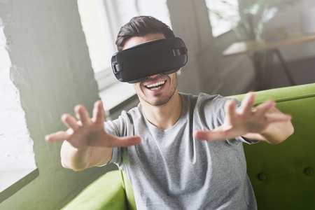 Close up portrait of astonished handsome guy experiencing virtual reality while using oculus rift headset for entertaining, sitting on couch at home. People, technology and innovation conceptの写真素材