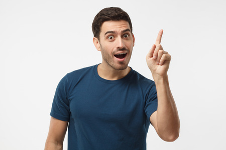 I got a solution! Photo of energetic nice smiling man wearing blue t-shirt isolated on gray background pointing finger in eureka sign, having great innovative idea, understanding の写真素材