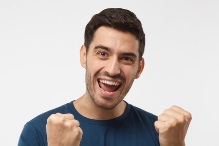 Young attractive male shouting while his team win, raised both fist in victory gesture, isolated on gray backgroundの写真素材