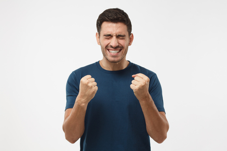 Closeup of emotional European man isolated on gray background showing white teeth while screaming with joy and victorious expression, holding hands in gesture of winner, looking extremely happyの写真素材