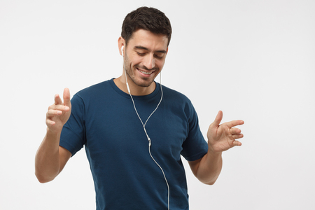 Young happy man smiling, listening music via headphones, dancing with closed eyes isolated on gray background. My favourite songの写真素材