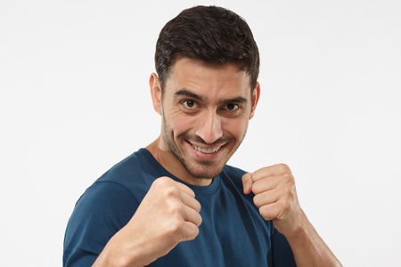 Close up portrait of smiling young guy keeping his fists ready to fight and defense himself. Strong sporty man boxing, looking at camera with smileの写真素材