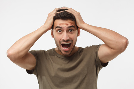 Headshot of handsome surprised manlooking at the camera, astonished with big sale prices, holding hands on head, standing against grey background. Human face expression conceptの写真素材