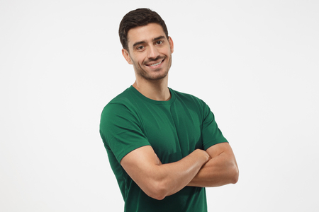 Portrait of attractive young sporty male in green t-shirt standing with crossed arms isolated on gray background. Fitness or crossfit trainerの写真素材