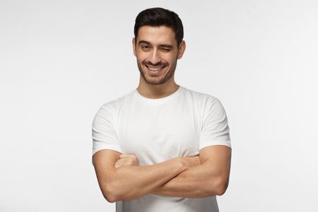 Handsome man with crossed arms smiling and winking, looking at camera isolated on gray backgroundの写真素材