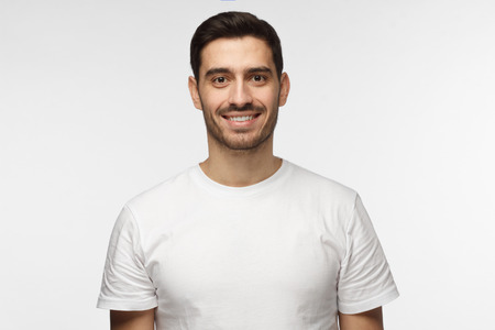 Young smiling optimistic man in blank white t-shirt standing isolated on light gray backgroundの写真素材