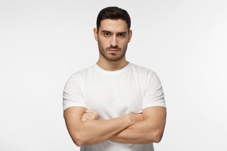 Closeup photo of young strong European Caucasian man pictured isolated on grey background dressed casually, standing with arms crossed and serious concentrated face at camera, looking aggressiveの写真素材