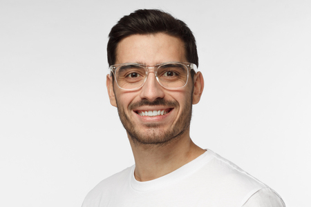 Studio portrait of confident European Caucasian man pictured isolated on gray background wearing casual clothes and plastic safety glasses showing happy friendly smile, willing to communicateの写真素材