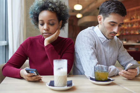 Bored couple experiencing problems in relationship, each staring at their own phoneの写真素材