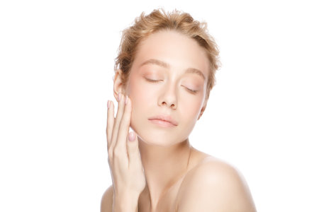 Beautiful blond woman face, eyes closed, touching her perfect clean skin with handの写真素材