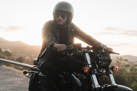 Young stylish biker sitting on his vintage motorcycle, wearing leather jacket and helmetの写真素材