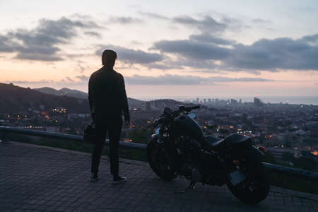 Silhouette portrait of biker or moto rider before sunrise standing near his bikeの写真素材
