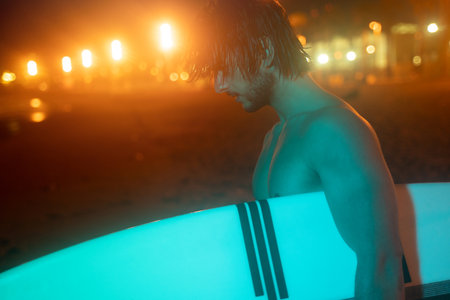 Neon green night portrait of surfer holding surf board and looking down, ready for surfingの写真素材