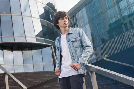 Attractive casual young student in jeans jacket standing on stairsの写真素材