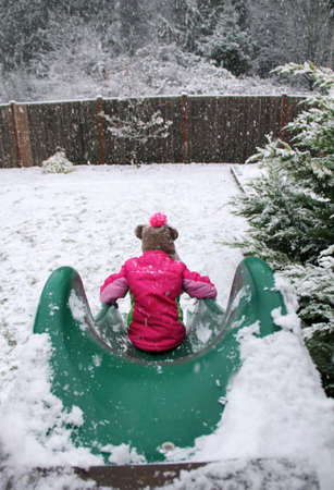 A little girl sliding down a slide in the snow.の写真素材