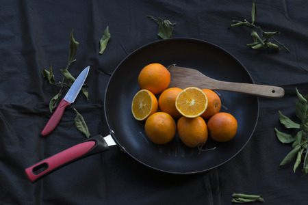 Oranges in the pan, black linen background, strewn with dead leavesの写真素材