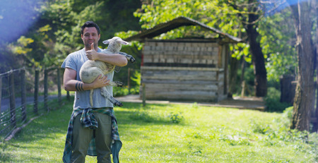 Young well-smiling farmer, he holds himself, against the backdrop of nature and a barn, the concept: ecology, livestock, farming, bio, nutrition.の写真素材