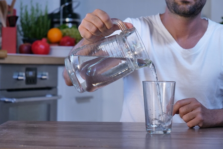 A smiling man in a white kitchen with a glass of water to purify his body, to relieve himself and to improve diuresis. Concept of: purity, cleansing and body care, diuresis.の写真素材