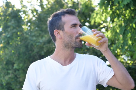 A man outdoors, immersed in nature, a glass of orange juice rich in vitamins and dietetic. A genuine fruit juice that is good for the body. Concept of: healthy drinks, diet, vitamins, regular lifeの写真素材