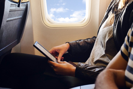 A woman on the plane uses the phone with the wi-fi present in flight. He relaxes on his comfortable seat and the clouds can be seen from the window. Concept of: travel, vacationの写真素材