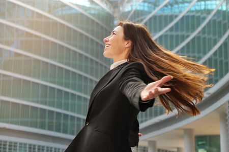 A businesswoman in a business suit, exulted by happiness after finishing the deal, in the background skyscrapers. Concept of: business, technology, economy and work and successの写真素材