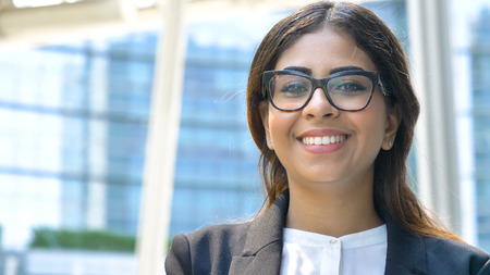 Portrait of young beautiful business woman (student) in suit, glasses, smiling, happy, walking down stairs, steps, on building background. Concept: new business, communication, Arab, banker, manager.の写真素材