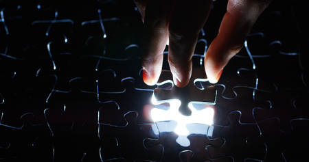 A creative completes the white puzzle putting the last missing piece. Concept: cooperation, teamwork, creativity, and access solution.の写真素材