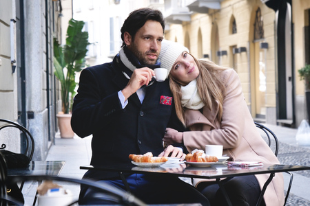 A couple of lovers have breakfast in a bar while sitting outdoors and looking at the phone. Concept of: love, valentine's day, technologyの写真素材