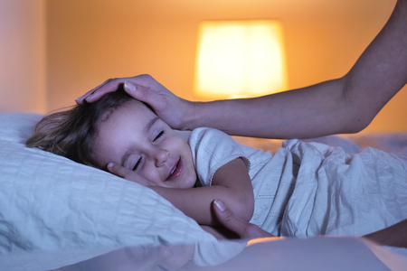 Goodnight mother and her daughter who sleeps at night in her bedroom and sees the moonlight coming through the window and lighting her sweet face. Concept of: peaceful dreams, family, relaxationの写真素材