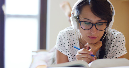 a girl lying on the bed listening to music while sending messages with your smart phone. concept of happiness and user friendly technology. connection with the technologicalの写真素材