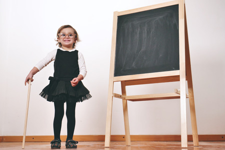A little girl dressed as a teacher in front of a small blackboard holding a lesson in economics, marketing, teamwork, mathematics. Concept of: educational, school, business and love for study.の写真素材