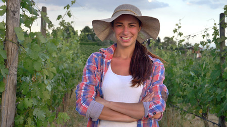 Beautiful smiling girl (woman) farmer looking over grape fields, in straw hat and in shirt, greens...