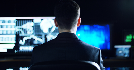 a young man controls the financial workflows and watch the monitors and writes to see stock quotes in his officeの写真素材