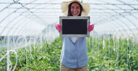 A beautiful girl in a straw hat and in pink gloves, holds a shovel for planting, in a greenhouse. Concept: bio products, natural products, fresh, delicious, fruits, vegetables, grow water plantsの写真素材