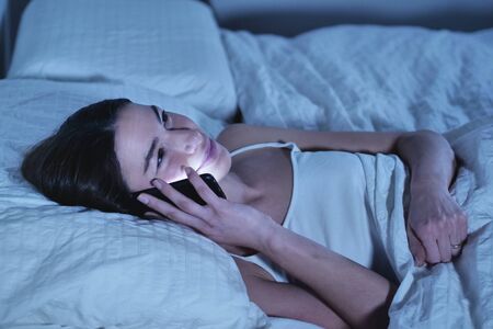 Beautiful woman in bed, send messages, watch social networks. Concept of: technology, network, relaxの写真素材