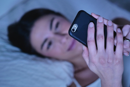 Beautiful woman in bed, send messages, watch social networks. Concept of: technology, network, relaxの写真素材