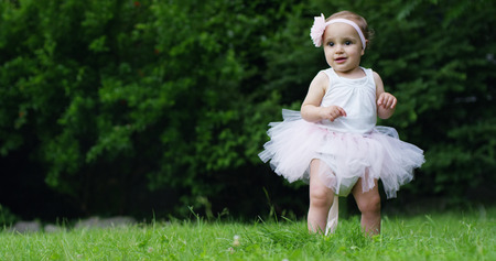 On a sunny spring day a toddler girl dressed as a dancer plays tries to stand up and take her first steps alone without a motherの写真素材