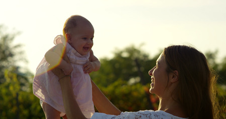 The young mother with her newborn baby girl in pink in a green garden. They have a lot of fun and joy. Concept of happiness, parenthood, carefree childhood and loveの写真素材