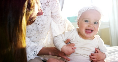 Mother and her little daughter with a white flower headband having fun in the bedroom in a lazy...