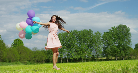 The young woman in pale pink dress is happy and carefree in a meadow with colorful balloons in her hands. Concept of happiness and freedomの写真素材