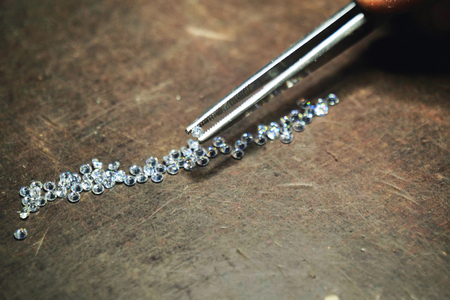Close-up of a goldsmith who with professional tweezers, checks the diamonds that he will use for the production of handmade luxury jewelery. Concept of: tradition, luxury, jewelry.の写真素材