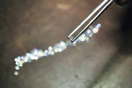 Close-up of a goldsmith who with professional tweezers, checks the diamonds that he will use for the production of handmade luxury jewelery. Concept of: tradition, luxury, jewelry.の写真素材