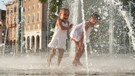 Two little girls are having fun in a fountain, smiling in white background.の写真素材